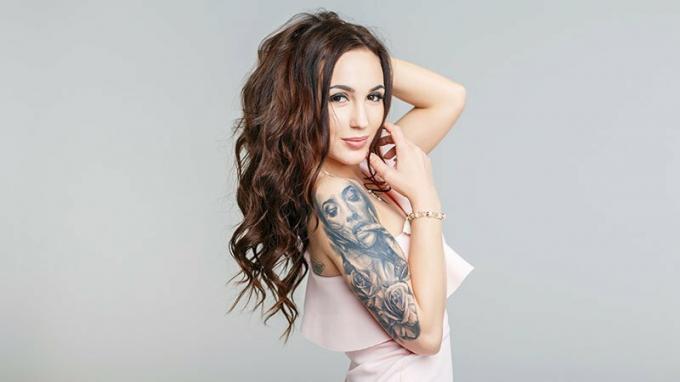 Hermosa mujer joven con elegante tatuaje en la mano en vestido rosa