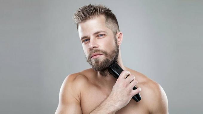 Pohľadný bradatý muž si zastriháva fúzy zastrihávačom