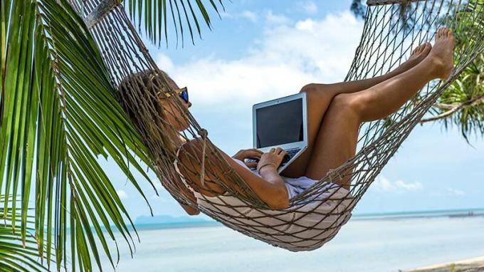 Nuori nainen kannettavan tietokoneen kanssa riippumatossa rannalla