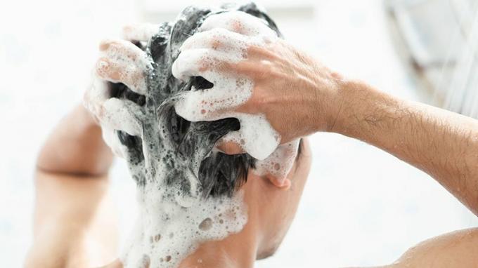 תקריב גבר צעיר שוטף שיער עם שמפו בחדר האמבטיה